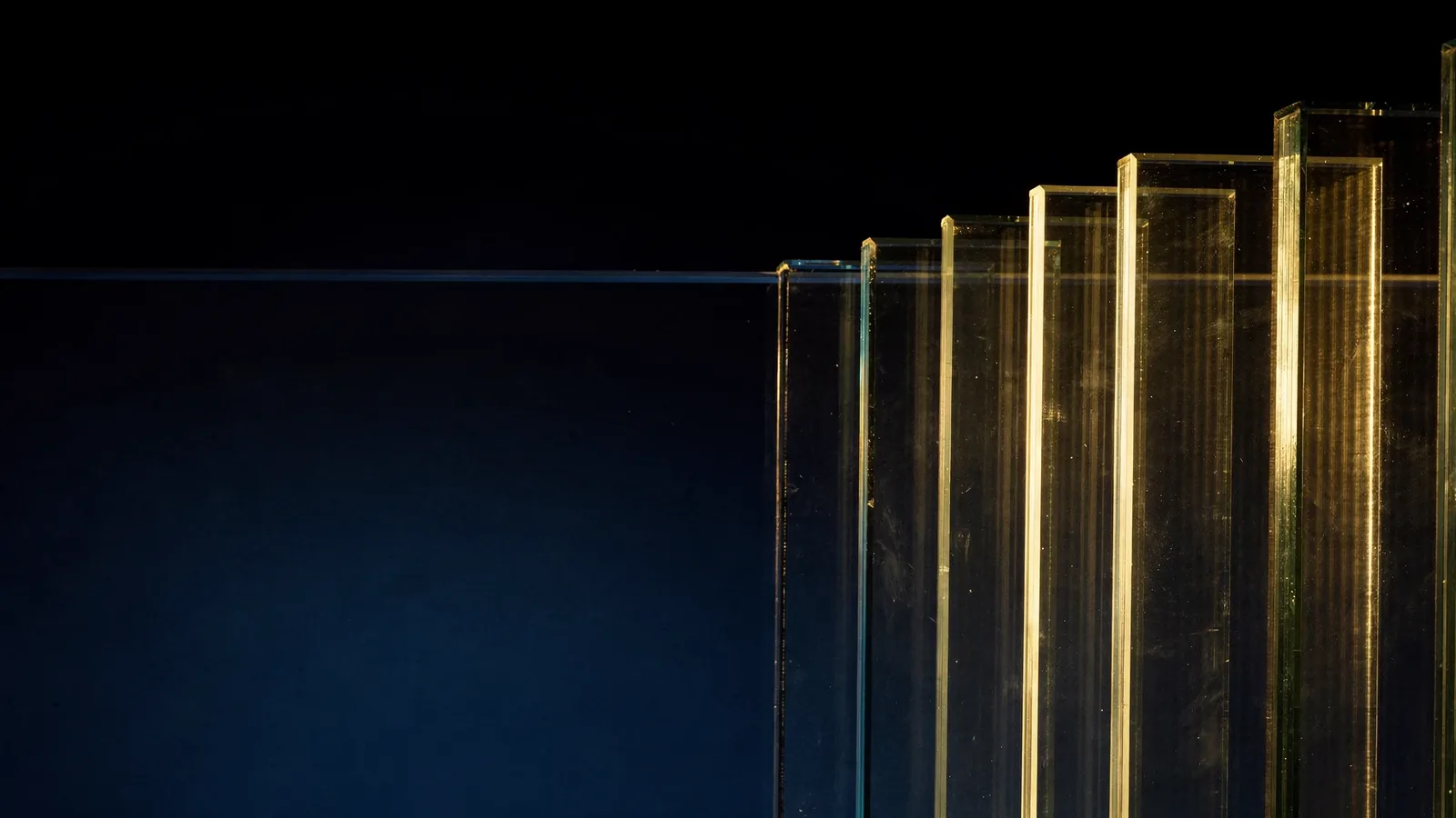 Sheets of clear glass in increasing thickness lit from the side, with edges turning greener as the glass gets thicker