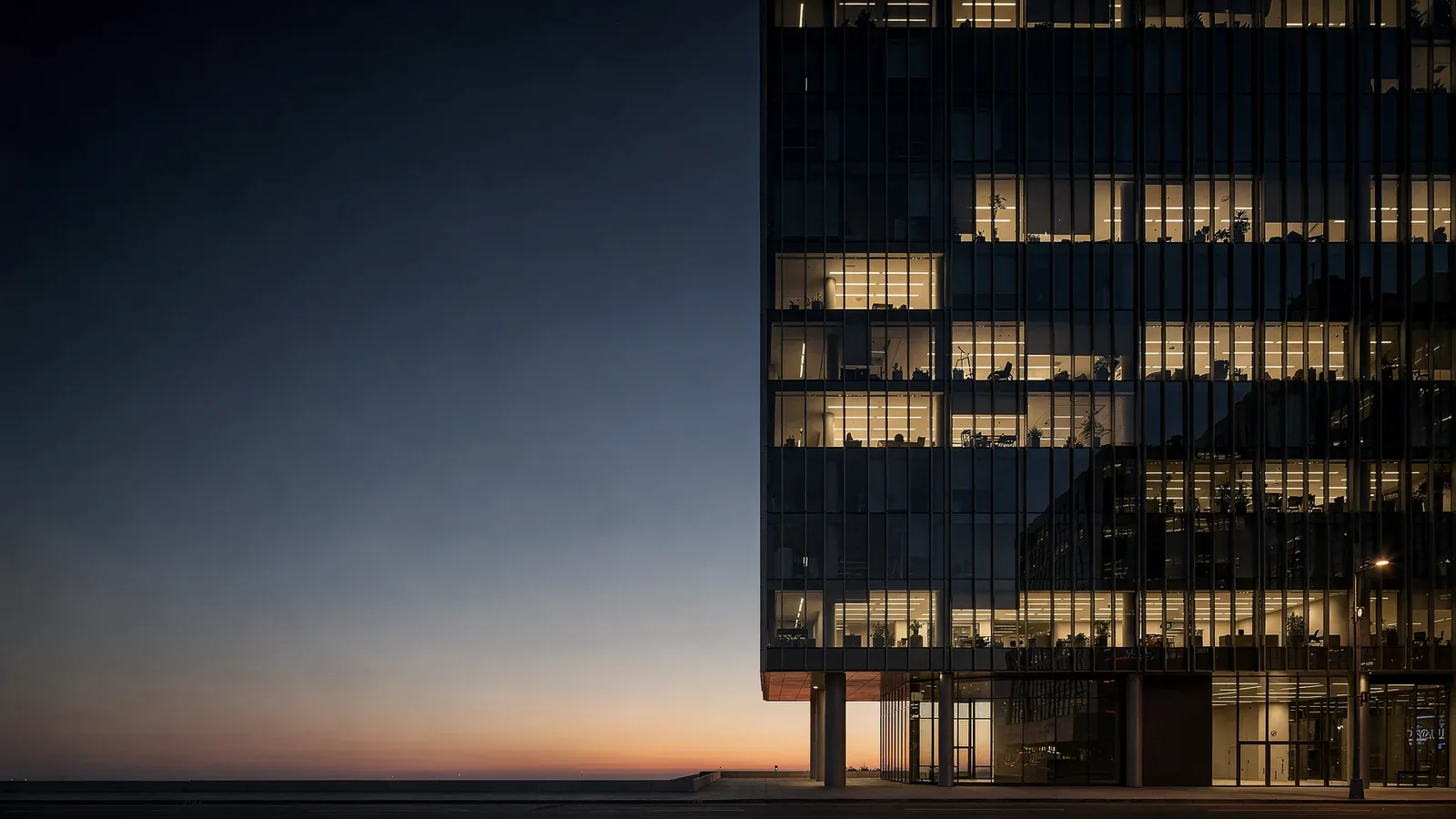 Glass office tower at dusk with lit vision glass on each floor and dark opaque spandrel bands between the floors